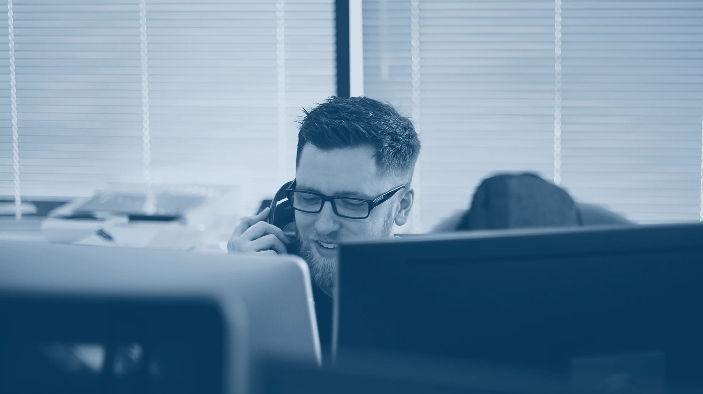 Homme d'affaires en costume travaillant dans un bureau moderne, souriant au téléphone devant plusieurs écrans d'ordinateur